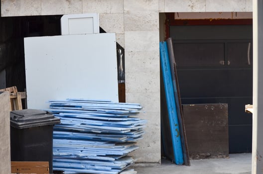 A stack of blue and white boards is piled up next to a closed garage door. The garage door is made of metal and has a black handle. The boards are of different sizes photo