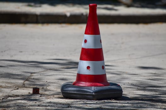 A red and white cone with black dots on it is sitting on the ground. The cone is a traffic cone and is placed in the middle of the road photo