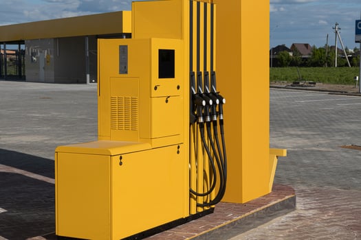 Fuel dispenser with multiple nozzles stands alone at a gas station, surrounded by open space and well-maintained surfaces under a clear sky photo