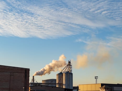 An industrial facility emits smoke into the sky as the sun sets, highlighting the contrast between nature and human activity photo