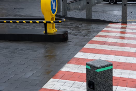 Wet pavement reflects surroundings while a yellow directional sign indicates traffic flow near a pedestrian crosswalk photo