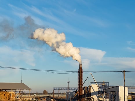 Thick white smoke rises from a factory chimney against a backdrop of a bright blue sky, capturing an industrial atmosphere in the late afternoon photo