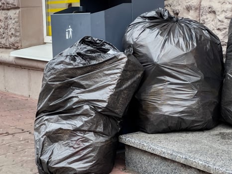Several black trash bags sit next to a waste bin on a busy urban sidewalk, showing signs of recent litter collection efforts photo