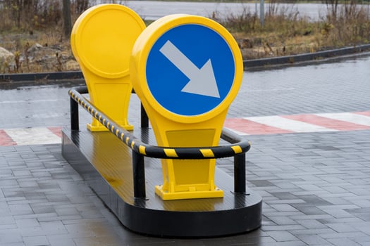 Bright yellow traffic signs direct vehicles toward the right in a well-paved area near a busy road under clear skies photo