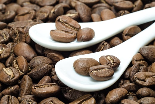 Beans of coffee in ceramic spoons on roasted coffee background photo