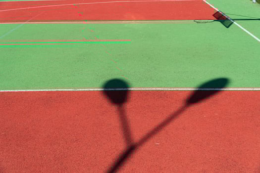 Striking shadows cast by nearby poles mingle with the bright colors of a freshly maintained tennis court on a sunny day photo