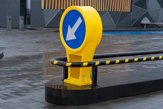 A vibrant yellow sign points downward as rainwater glistens on the pavement of a contemporary parking facility in an urban setting photo