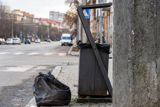 A garbage container stands near the sidewalk, surrounded by black trash bags, highlighting urban waste management challenges photo