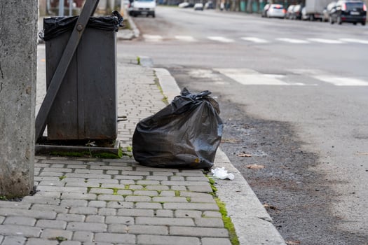 A pile of discarded black trash bags rests on the pavement next to a recycling bin on a city street in the early morning time photo