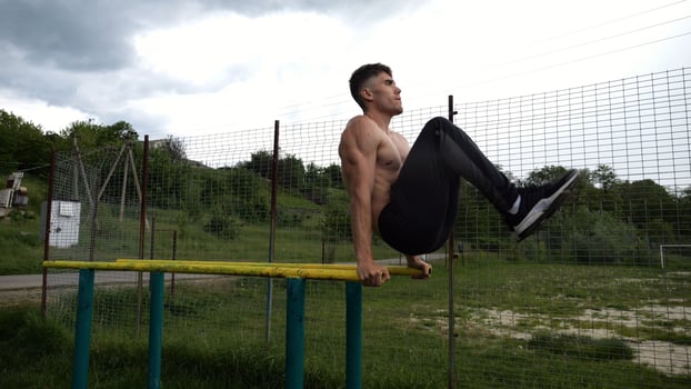 Strong guy training abdominal muscles on parallel bars at sports ground. Young shirtless sportsman exercising at nature. Sporty athlete working out at nature. Concept of active sportiv lifestyle photo