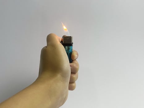 Hand holding a burning lighter against a white background in a studio shot photo