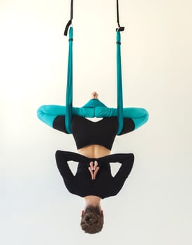 Caucasian woman practicing fly yoga bat asana over white background in fitness studio, copy space, back view. Health, sport, yoga concept photo