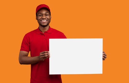 Advertisement Concept. Portrait of smiling african american male courier holding empty blank board isolated on yellow orange studio background. Black guy recommending delivery service photo