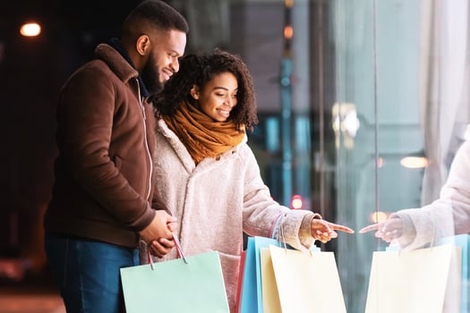 Look Here. Beautiful african american woman showing to her man fashion clothes in shop window, walking in the evening near shopping centre. Winter Sales And Discount, Retail, Purchase photo