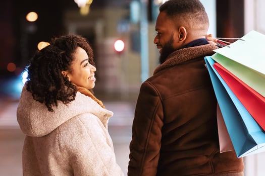 Happy Loving Family. Back rear view portrait of smiling african american man and woman looking at each other, carrying shopping bags and holding hands while walking near mall in the evening photo