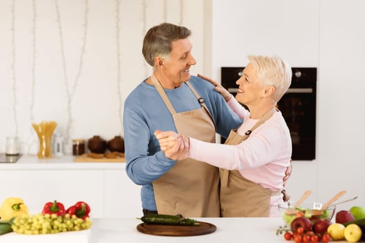 Cheerful Elderly Couple Dancing In Modern Kitchen Enjoying Dinner Preparation And Having Fun At Home On Weekend. Senior Family, Retirement Happiness And Relationship In Older Age Concept photo