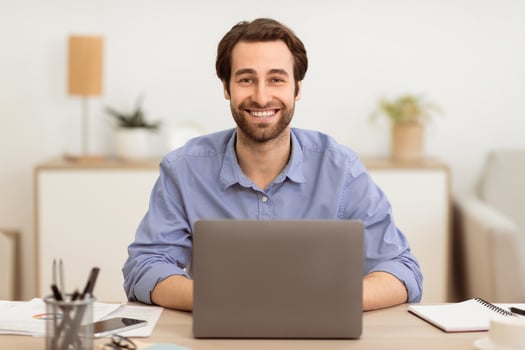 Successful Businessman Sitting At Laptop At Workplace, Smiling To Camera Working On Computer Online In Modern Office. Business Career, Entrepreneurship Concept. Selective Focus photo