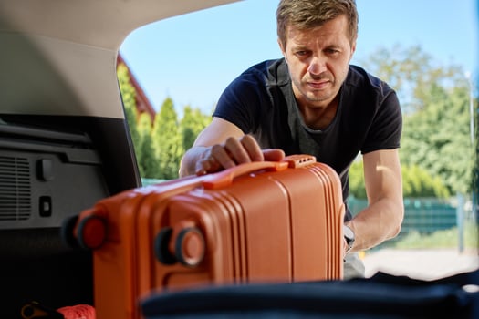 Man loading orange suitcase into open car trunk, inside view. Concept of travel preparation, packing for vacation or departure on road trip photo