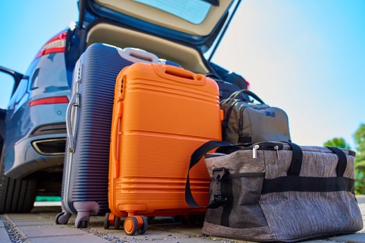 Suitcases and bags in front of open car trunk, standing on pavement near suburban house. Luggage ready for loading in vehicle before travel or moving. Concept of relocation or road trip photo