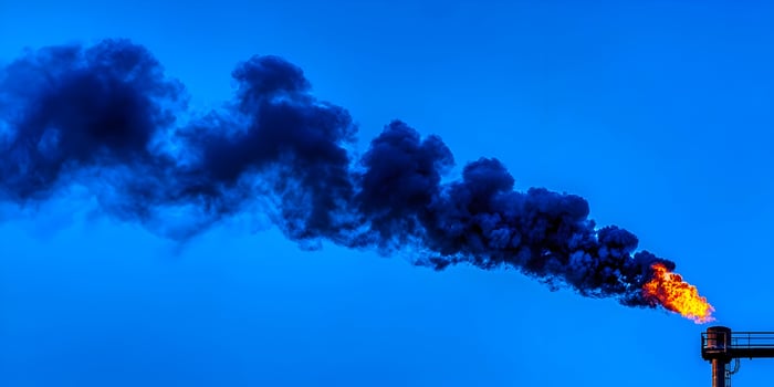Industrial Smokestack Black Smoke and Orange Flame Against Blue Sky photo