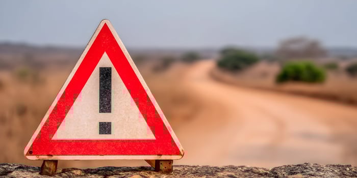 Red Triangle Warning Sign on Rock with Blurred African Road Background photo