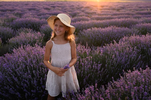 Young girl twirling in a lavender field, hat flying as golden sun sets. photo