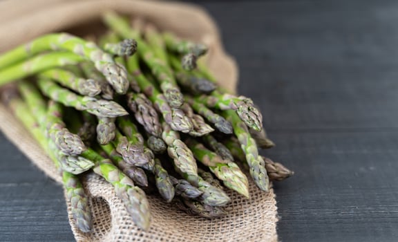 A bundle of green asparagus on a dark wood surface with coarse sackcloth, evoking a farm-fresh feel. photo