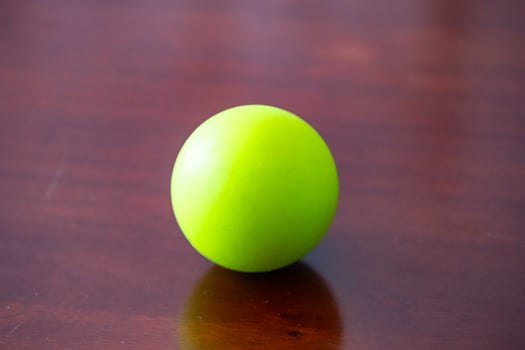 A vibrant green sphere resting on a polished wooden surface. isolated photo