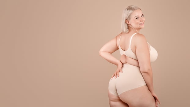 Body Positive. Beautiful Curvy Woman Posing In Underwear Over Beige Studio Background, Attractive Plus Size Blonde Female In Lingery Standing Half-Turned And Smiling At Camera, Copy Space photo