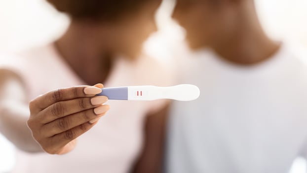 Closeup of positive pregnancy test in unrecognizable black woman hands cuddling with her husband. African american couple will become parents, showing pregnancy test, selective focus photo
