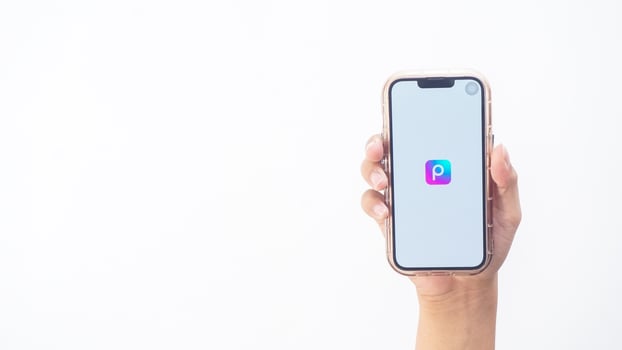 Yogyakarta, Indonesia, 2025 - Hand holding smartphone that shows Picsart application icon, a creative editing platform, on the screen isolated on white background photo