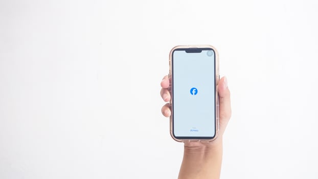 Yogyakarta, Indonesia, 2025 - Hand holding smartphone that shows opening page of Facebook application, a social networking service platform, on screen isolated on white background photo