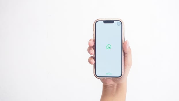 Yogyakarta, Indonesia, 2025 - Hand holding phone that shows front page of WhatsApp application, a communication platform, on the screen isolated on white background photo