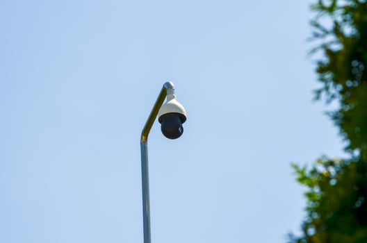 A street light with a camera on top of it. The camera is black and white. The sky is blue and clear photo