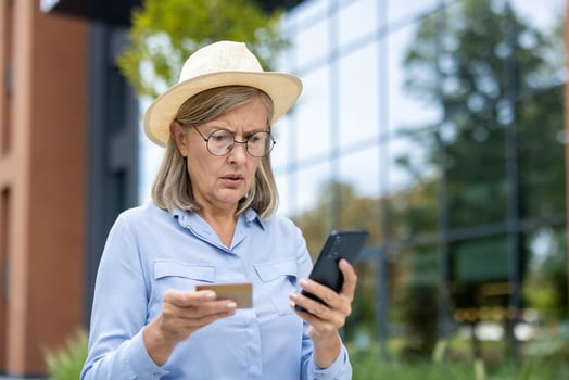 An older woman is looking at her credit card and smartphone in confusion, possibly experiencing online transaction issues. photo
