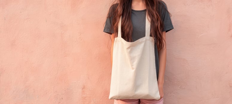 The woman holding a tote bag against a textured pink wall. photo