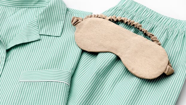 Beige eye mask for sleep on folder striped green pajama, close up texture fabric, minimal lifestyle aesthetic banner. Top view woman sleeping mask for comfort rest, healthy trend, stylish sleepwear photo