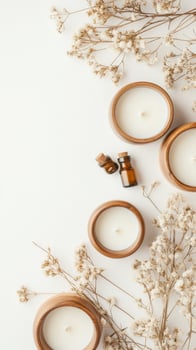Aroma bottles and burning wax candles in wooden jars with dried floral accents against light background. Spa concept. Top view flat lay photo