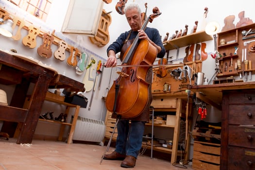 mature violin maker craftsman playing a newly made viola using the bow to hear the sound at the workplace photo