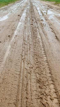 A dirty country narrow road. After the rain, puddles, mud and tire marks formed on the road. Shot on a phone photo