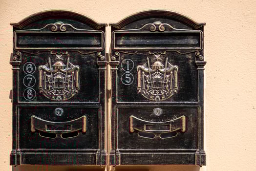 Vintage-style metal mailboxes mounted on a wall. Each box features ornate decorations with a crest. photo
