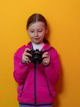 Smiling girl holding vintage camera against orange background photo
