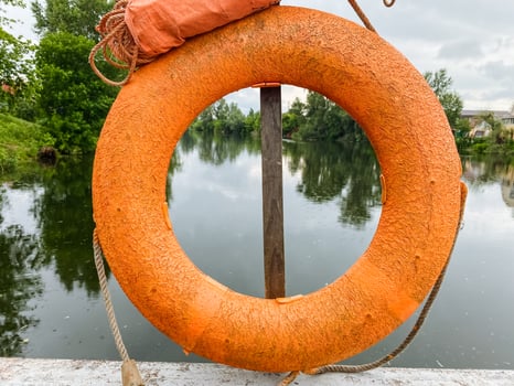 An orange life preserver, often used for safety, is currently hanging on a sturdy pole that is positioned conveniently near a large body of water where people can swim and relax photo