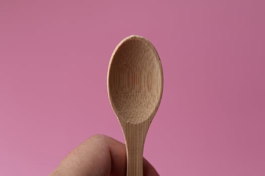 Hand holding Old Wooden Spoon on pink background photo