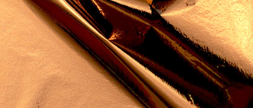 Elegant bronze foil texture with a glossy, holographic finish. Wrinkled, creased folds creating a photo