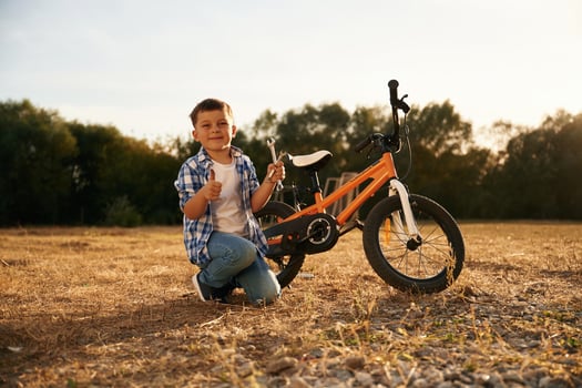 Holding wrench. Cute boy, is with, his bicycle on the field photo