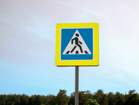 A road sign in the pedestrian crossing area against the sky. A warning about a pedestrian crossing. A reminder to follow the rules of the road. Pedestrian safety. photo