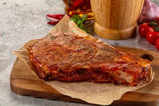 A piece of meat on a cutting board next to a bottle of whiskey photo