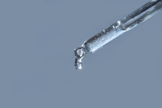 Close-up of transparent liquid drop from glass pipette against light blue background. photo