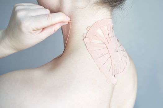 Female applying therapeutic tape on upper back for pain relief and posture correction. photo